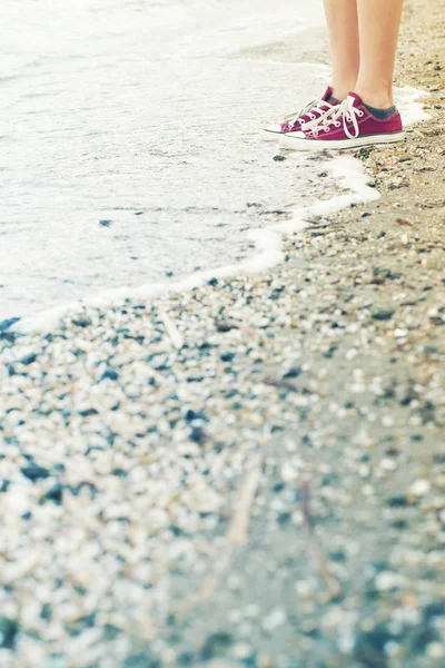 Voeten van het kind van de tiener in gym schoenen op een zee-strand in een zomerdag — Stockfoto