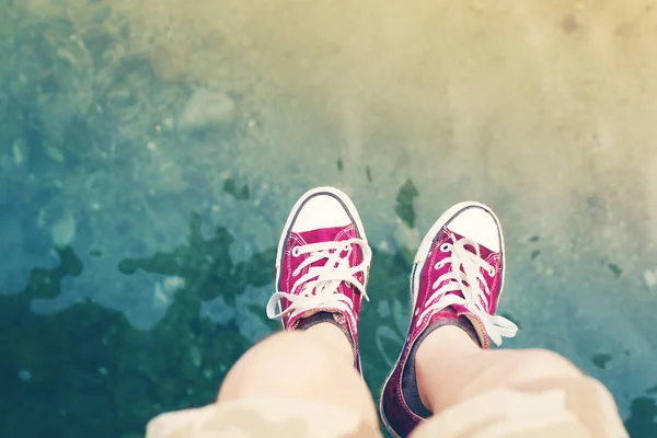 Voeten van het kind van de tiener in claret sneakers tegen de achtergrond van de zee — Stockfoto