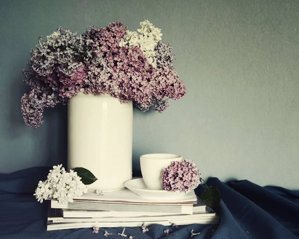 Kytice fialová bílá váza, šálek čaje a hromadu časopisů, výzdoba ve stylu vintage. Jarní Romantický kytice pro vaši dovolenou. — Stock fotografie