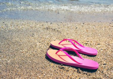 Bir yaz güneşli günde bir plajda denize karşı pembe flip flop