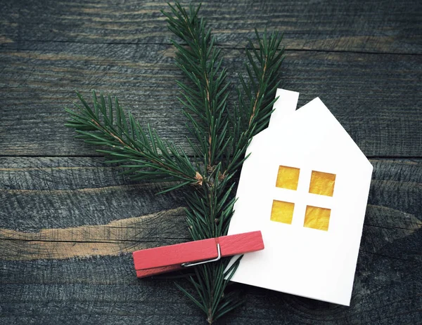 Decorative Christmas house from white paper and a fir-tree branch on a textural wooden board. — Stock Photo, Image