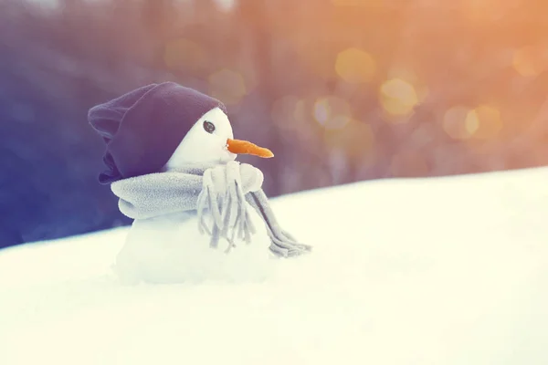 Pequeño muñeco de nieve en una gorra y una bufanda en la nieve en invierno . —  Fotos de Stock