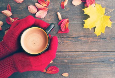 Eller kırmızı örme eldivenler ve parlak sonbahar yaprakları ile ahşap bir gemide sütlü kahve