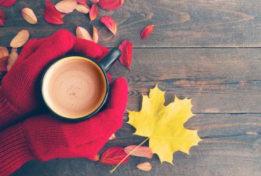 Eller kırmızı örme eldivenler ve parlak sonbahar yaprakları ile ahşap bir gemide sütlü kahve