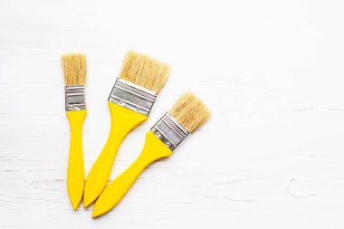 Three wooden yellow paint brushes on a white wooden board, top view