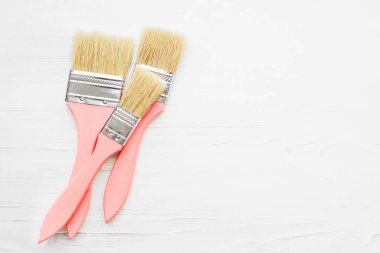 Three wooden pink paint brushes on a white wooden board, top view