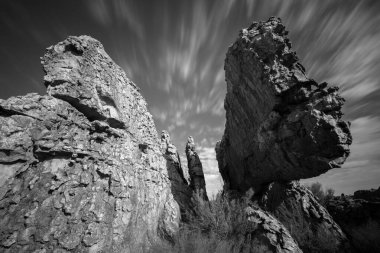 Ön planda büyük kaya oluşumları ve gökyüzünde hızla hareket eden bulutlarla dolu, Güney Afrika 'daki Cederberg dağlarından alınmış, simsiyah ve beyaz bir manzara..