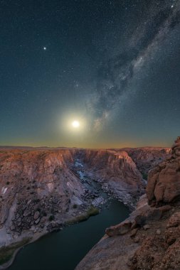 Derin mavi gökyüzünde Ay 'ın yükseldiği, Güney Afrika' daki Augrabies Falls Ulusal Parkı 'ndaki nehir ve dağların manzaralı görkemli bir dikey gece gökyüzü fotoğrafı..