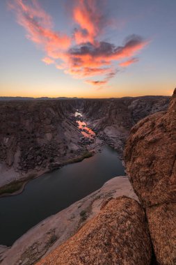 Günbatımından hemen sonra mavi gökyüzünde pembe ve sarı bulutlarla birlikte Güney Afrika 'daki Augrabies Falls Vadisi' nin, dağların ve nehrin güzel dikey manzarası..