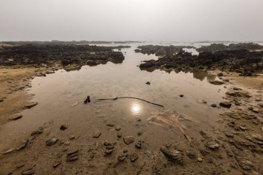 Gün doğumunda deniz kıyısında sakin bir deniz manzarası. Güneş bulutlardan süzülüyor ve Güney Afrika 'nın Nolloth Limanı' ndan alınan suyun yüzeyine yansıyor..