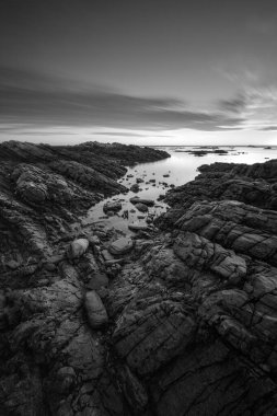 Port Nolloth, Güney Afrika 'da gün batımında çekilen sakin, siyah beyaz deniz manzarası. Önplanda dramatik bulutlu bir mavi ve kayalar var..