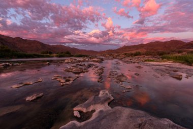 Gün batımından sonra, Richtersveld Güney Afrika 'sında çekilen su yüzeyine çarpıcı turuncu bulutların yansıdığı, dağlarla ve Orange Nehri' yle çekilen güzel, uzun bir manzara..