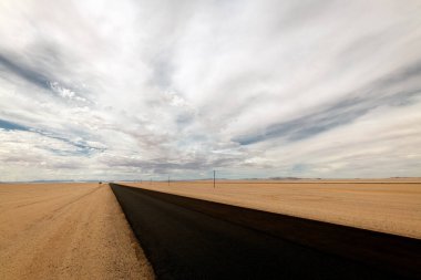 Luderitz, Namibya yakınlarında çekilmiş ürkütücü bir çöl manzarası milli katran yolu, ön planda çöl kumu, fırtınalı, karamsar, gökyüzünde bulutlar..