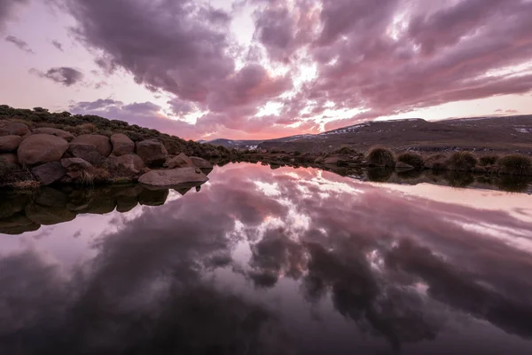 Lesotho Dağları 'nın kardaki gölünün akşam erken saatlerinde çekilmiş güzel bir fotoğrafı. Pembe fırtınalı bulutlar suda inanılmaz yansımalar yaratır..