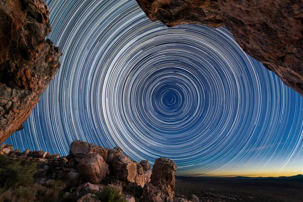 A beautiful night sky photograph with circular star trails framed by dramatic rocks in the foreground, taken in the Cederberg mountains in the Western Cape, South Africa.