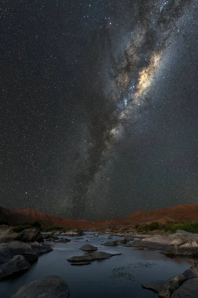 Samanyolu ve galaktik merkezi ile güzel bir dikey gece manzarası, ve önplanda Orange Nehri ve ufukta dağlar, Richtersveld Ulusal Parkı, Güney Afrika.