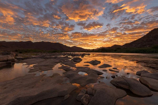 Gün batımından sonra, Richtersveld Güney Afrika 'sında çekilen su yüzeyine çarpıcı turuncu bulutların yansıdığı, dağlarla ve Orange Nehri' yle çekilen güzel, uzun bir manzara..