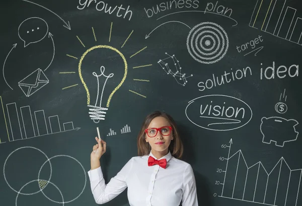 Jonge zakenvrouw wijzend op de gloeilamp op schoolbord — Stockfoto