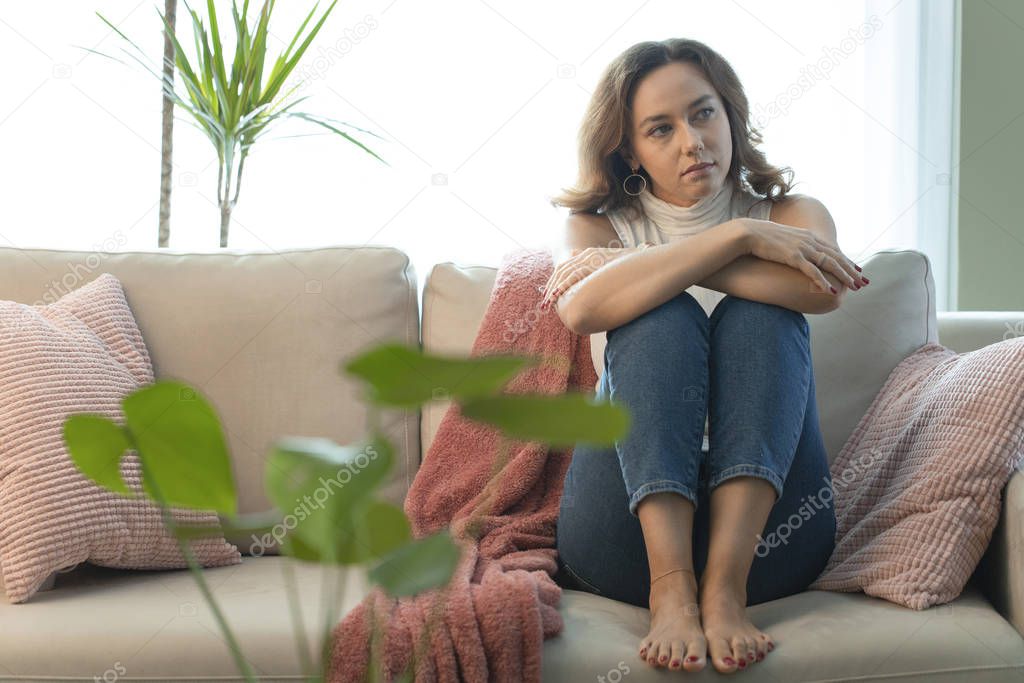 Thoughtful young woman sitting on sofa alone at hom