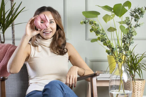 Mladá žena se usmívá pohledem přes růžové koblihy na oku — Stock fotografie
