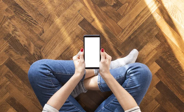 Mujer joven sentada en el suelo en casa y usando un teléfono móvil — Foto de Stock
