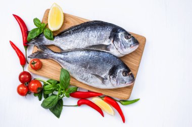 Çiğ dorado ahşap kesme tahtası üzerinde beyaz masada sebzeli balık. Üstten Görünüm