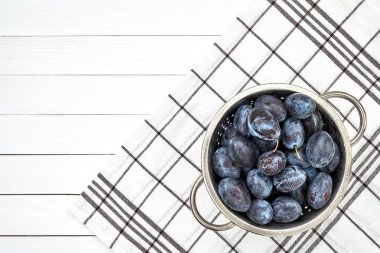 Beyaz ahşap masa üzerinde kevgir içinde mor Erik. Üstten Görünüm