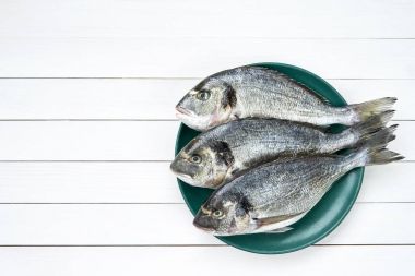Çiğ dorado balık beyaz masada yeşil plaka üzerinde. Üstten Görünüm, kopya alanı
