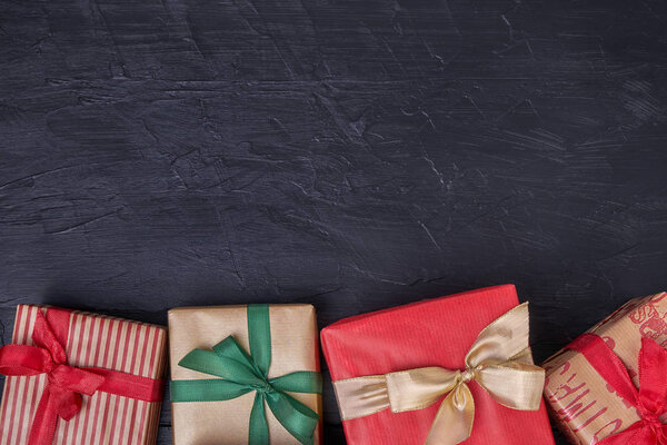 Упакованные подарочные коробки украшены лентой на черном деревянном фоне. Копирование пространства, вид сверху
