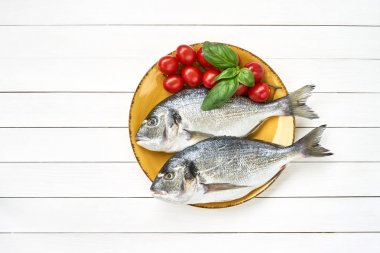 Fresh dorado fish on yellow plate with tomatoes on white wooden table. Top view, copy space. clipart