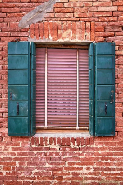 Window with green shutters on red brick wall of houses. Italy, Venice, Burano.