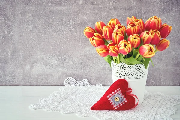 Czerwone tulipany bukiet w biały wazon ozdobiony czerwony tkanina usłyszeć — Zdjęcie stockowe