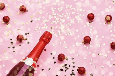 Noel kutlamalarının yatağı. Pembe arka planda Noel süslemesi olan şampanya şişesi. Üst görünüm, alanı kopyala.