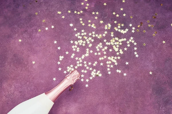 Botella de champán con confeti dorado sobre fondo púrpura. Piso laico de concepto de celebración navideña. Copiar espacio para texto . — Foto de Stock