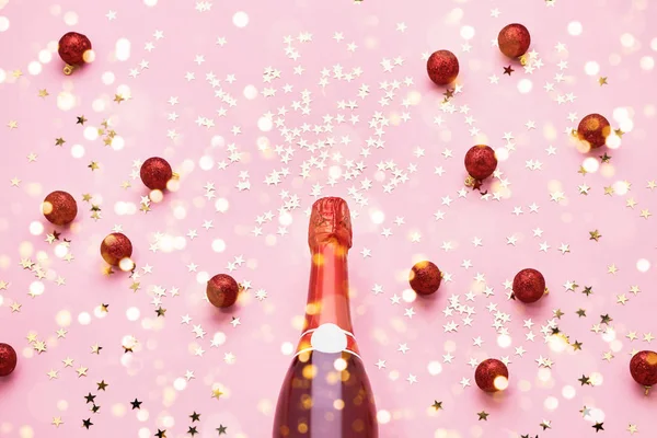 Botella de champán con decoración roja de Navidad sobre fondo rosa. Vista superior, espacio de copia — Foto de Stock