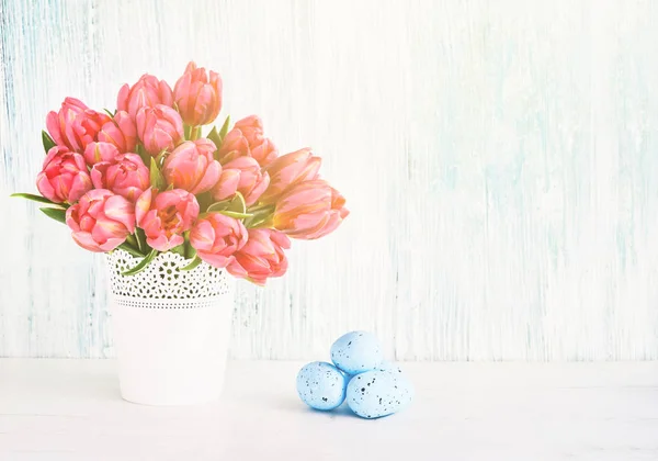 Easter background. Decorative Easter blue eggs and pink tulips in vase. Copy space for text. Easter celebration concept.