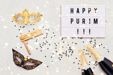Işık kutusunda mutlu Purim yazıları ve iki şampanya şişesi, karnaval maskesi ve ışık arka planında gragger. Purim Karnavalı 'nın düz yatışı konsepti. Üst görünüm, boşluğu kopyala. Tatil arkaplanı