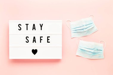 Tıbbi koruyucu maske ve pembe arka planda ışık kutusuna yazılmış güvenli bir yer. Sağlık ve tıbbi konsept. Üst görünüm, metin için boşluk kopyala. Karantina konsepti.