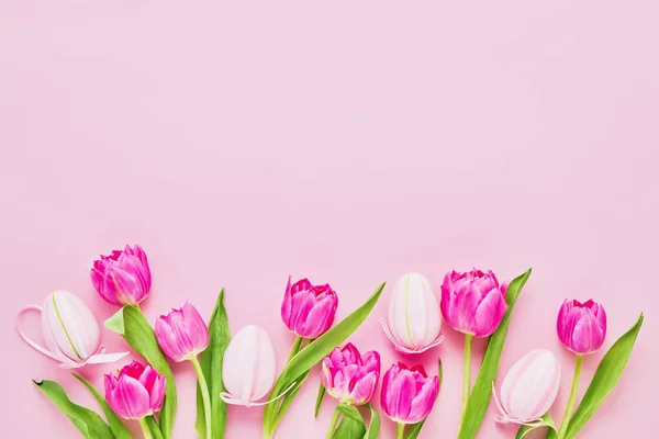 Easter background. Decorative pink Easter Eggs and tulip flowers on pink background. Top view, copy space for text. Easter celebration concept.