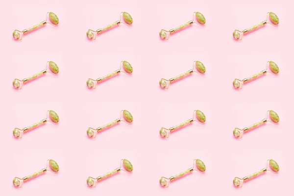 Seamless pattern. Massage roller for face with two jade stone on pink background. Skin care concept. Copy space, top view.