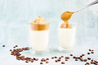 Moda ev yapımı mavi arka planda cam kaplı Dalgona kahvesi. Popüler Kore kahvesi tarifi. Yanında da köpüklü kahve. DIY, talimatlar.