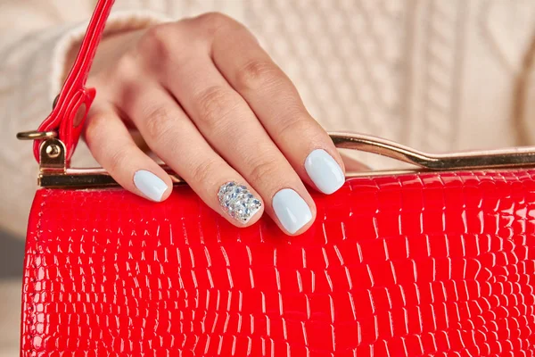 Primo piano di una manicure di donne azzurro pallido su borsa rossa . — Foto Stock