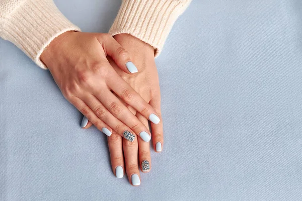 Beautiful female manicure on blue fabric background.