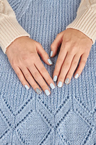 Delicate blue manicure with rhinestones on knit background.