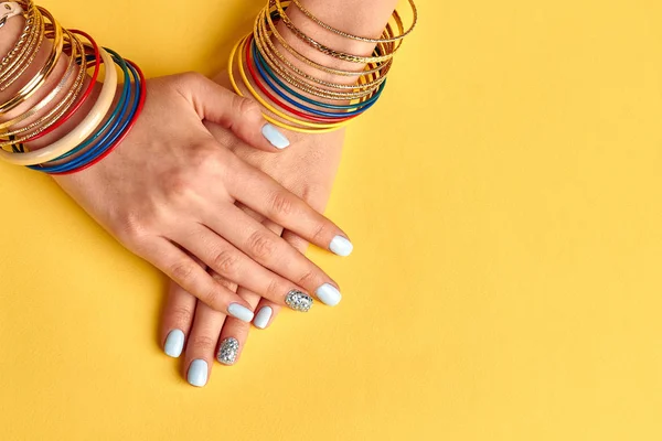 Bella manicure blu con cristalli su sfondo giallo . — Foto Stock