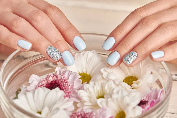 Close-up of a blue manicure with delicate flowers in a bowl.