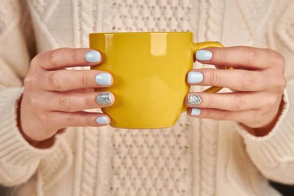 Belle mani femminili con manicure blu che tengono una tazza gialla . — Foto Stock