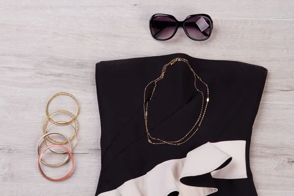 Zwarte jurk met zonnebrillen en sieraden op een houten achtergrond. — Stockfoto