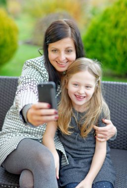 Anne ve kızı doğada oturan ve selfie konuşuyor 