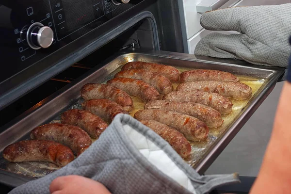 Из духовки достают поднос с горячими домашними колбасами. — стоковое фото